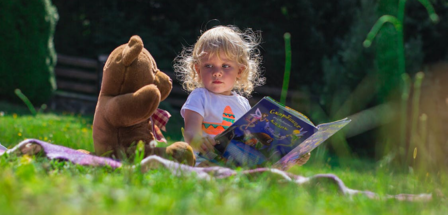 A girl reading a book alongside a teddy
