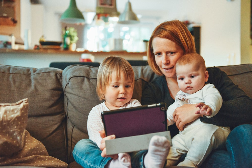 A woman watching a tablet with two kids