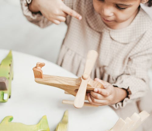 A Toddler is Playing a Wooden Airplane