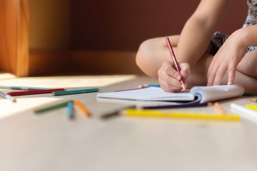 Kid writing in a notebook with colored pencils.