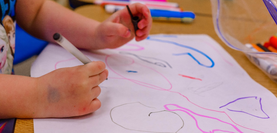 A kid drawing on a paper with markers.
