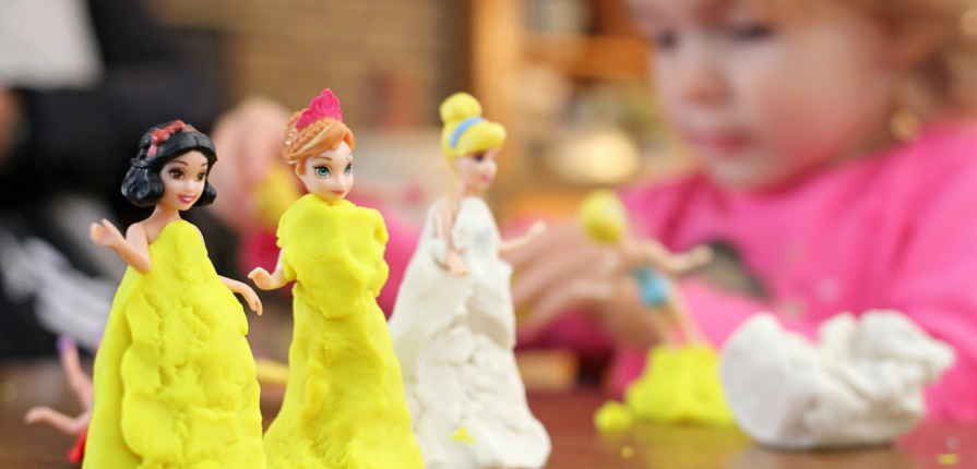 Little girl dressing up dolls in playdough