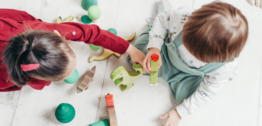 Preschoolers immersed in imaginative play with wooden dinosaur toys, exploring creativity and social skills, highlighting positive interactions in disciplining a toddler's developing behavior.