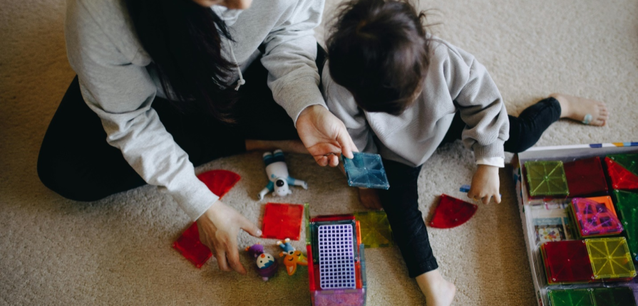 A mother and child happily playing with magnetic multi-colored blocks on a carpeted floor, yet another one of the best educational toys of 2024 for younger children.