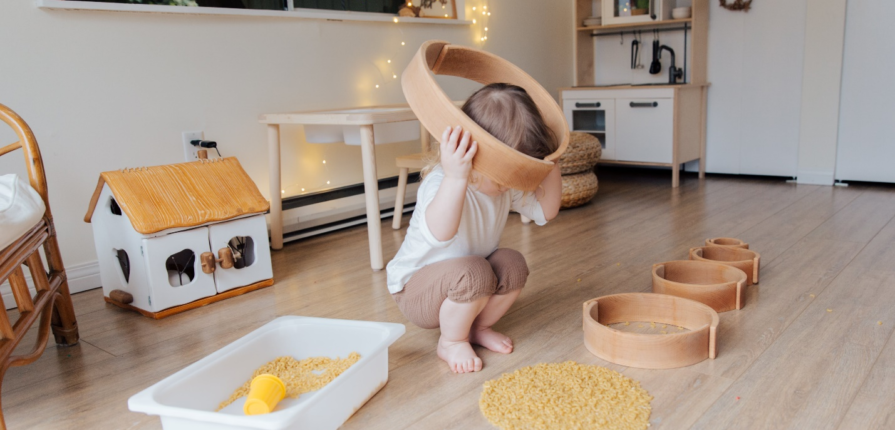 A toddler engrossed in playful exploration with circular structures and macaroni in a Montessori environment, an engaging activity for toddlers.