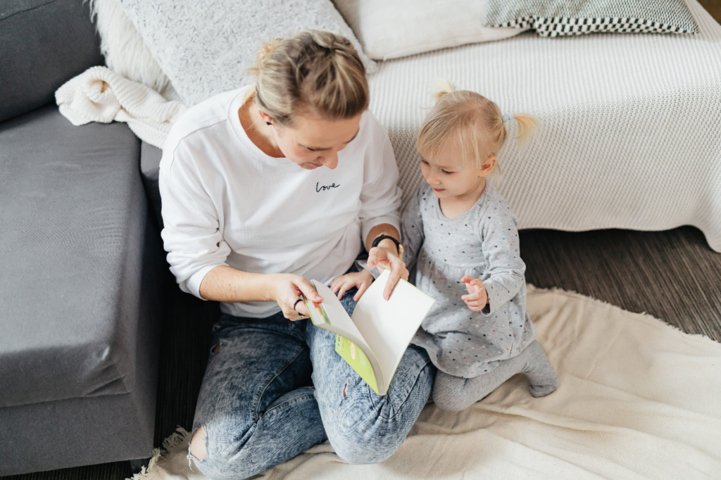 A toddler sitting on a throw beside a parent, immersed in a book, showcasing active engagement for children in a cozy home setting.