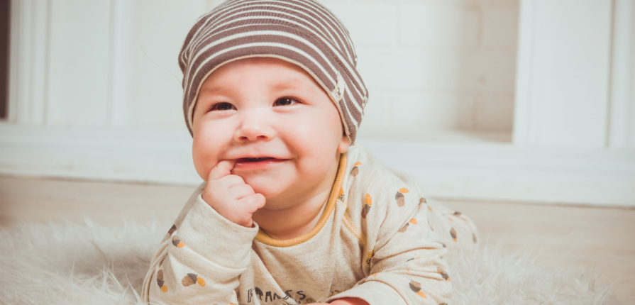 An adorable infant lies on a soft shag rug, smiling and exploring the world with a finger in the mouth—a delightful moment in baby communication.