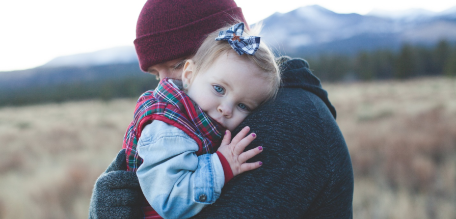 A toddler in winter attire, nestled warmly in her father's arms outdoors, exemplifying active engagement for children through loving, seasonal connection.