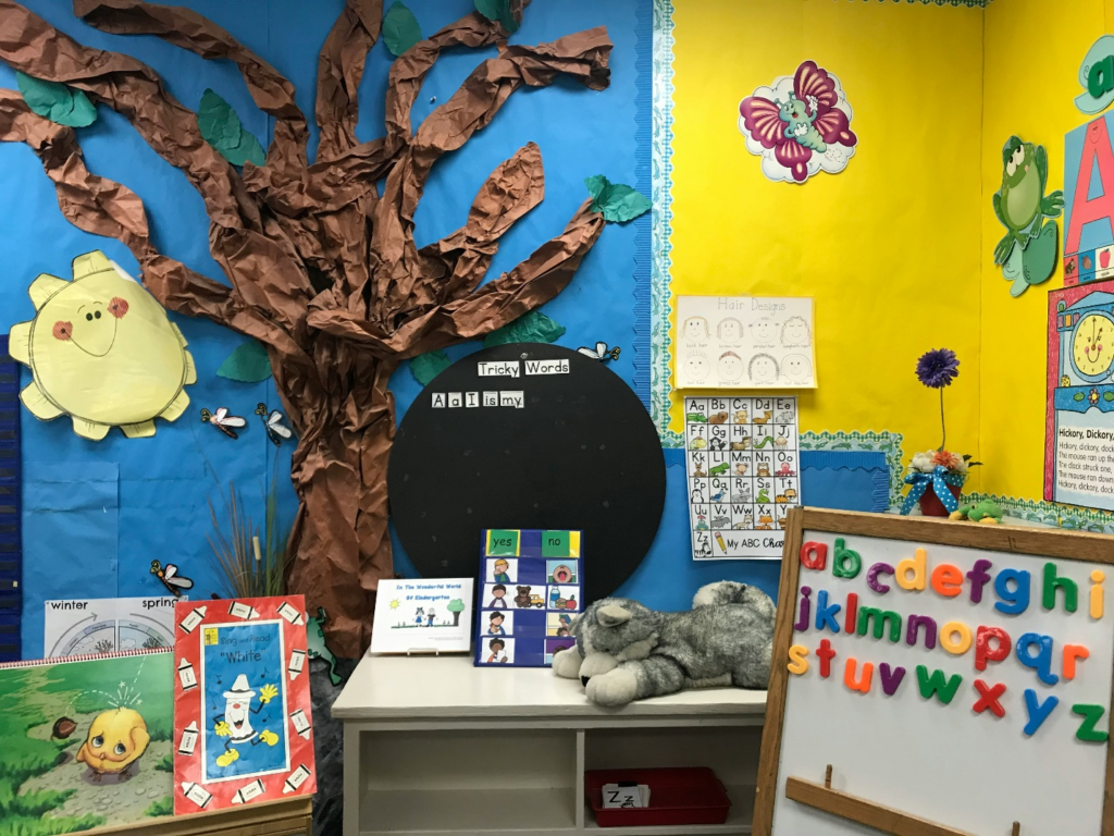 a preschool classroom with colorful decorations, including a tree, a Tricky Words board, and alphabet magnets