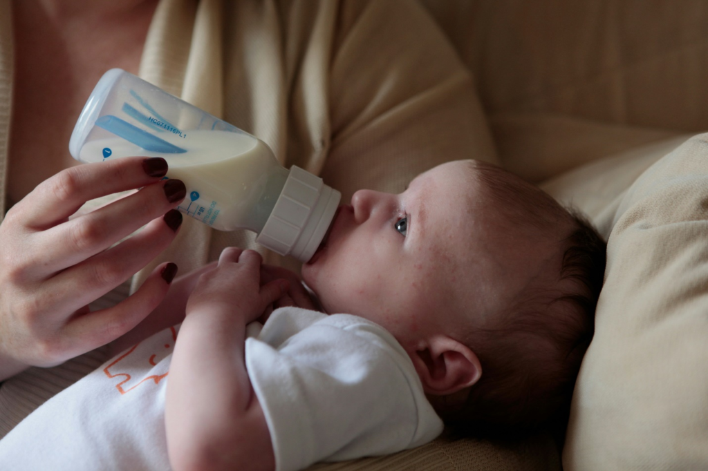  Caregiver holding an infant and feeding via bottle, following infant feeding cues at daycare