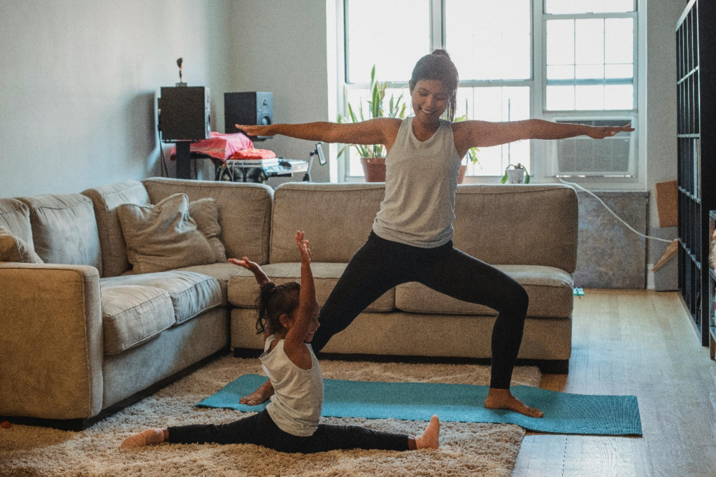 A mother and child holding toddler-friendly yoga poses on a shaggy carpet in a cozy living room.