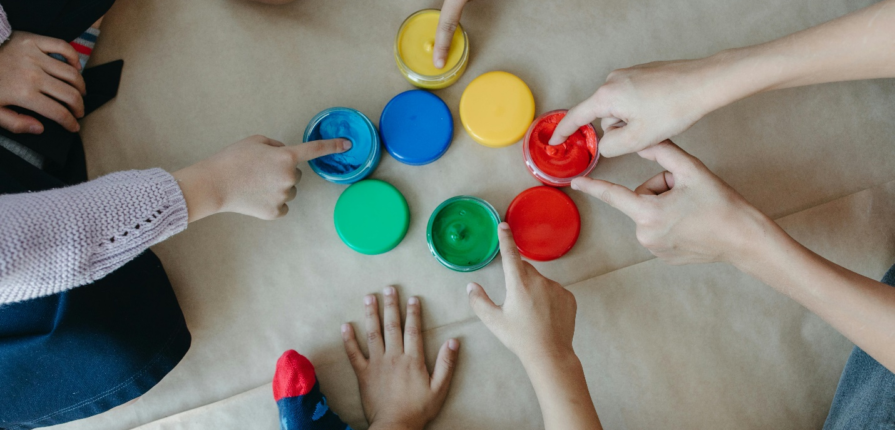 Six little hands reaching out to touch vibrant playdoughs in a circle on the floor, making sensory play for toddlers an exciting adventure.