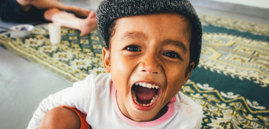 A toddler screaming with an ethnic carpet in the background, showcasing the range of toddler emotions that can be managed with the help of positive parenitng tips