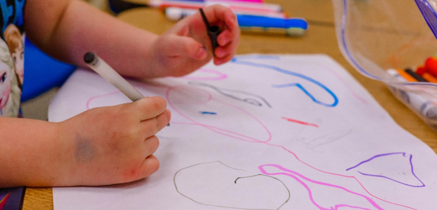 A child drawing on white paper with colored pens.